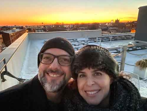 Silvia Acevedo and Jeff Miracola smiling with snow and a colorful sunset behind them