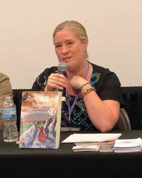 Photo shows author Valerie Biel and her book titled Circle of Nine Beltany. Valerie is white, blonde, and has her hair pulled back into a low ponytail.