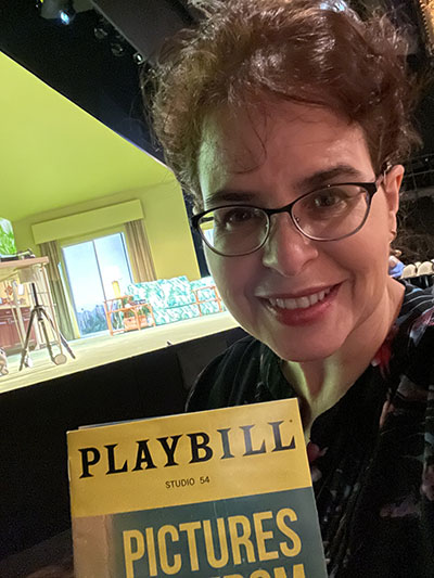 Photo shows Silvia Acevedo holding the playbill for the Broadway play Pictures from Home staring Nathan Lane, Danny Burstein, and Zöe Wanamaker