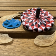 Image shows two spinning tops, a flat blue spinner and a white, black, and white spinner on a table with some maple helicopter seeds.