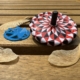 Image shows two spinning tops, a flat blue spinner and a white, black, and white spinner on a table with some maple helicopter seeds.